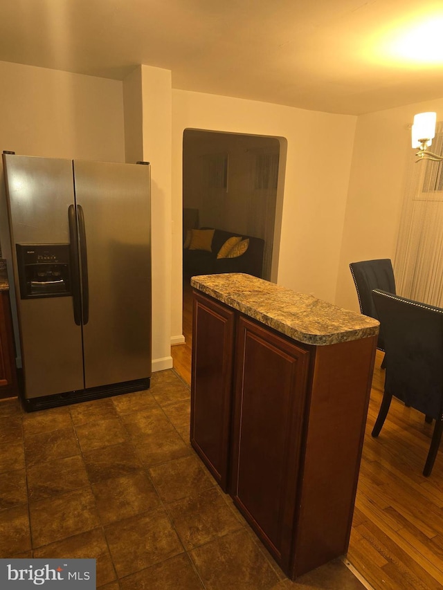 kitchen with light stone counters, stainless steel refrigerator with ice dispenser, and dark brown cabinets