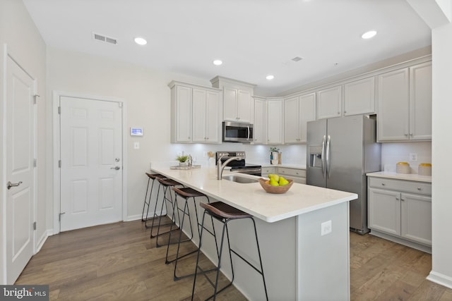 kitchen featuring visible vents, appliances with stainless steel finishes, wood finished floors, a peninsula, and a kitchen bar
