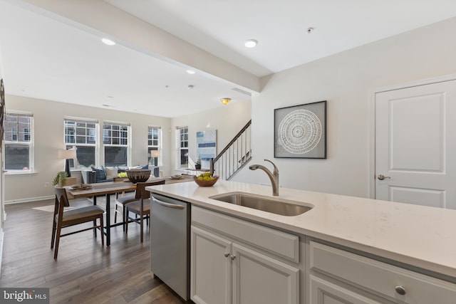 kitchen with light stone counters, dark wood-style flooring, stainless steel dishwasher, open floor plan, and a sink