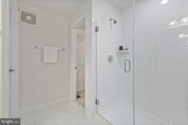 full bath featuring a walk in closet, a shower stall, baseboards, and tile patterned floors