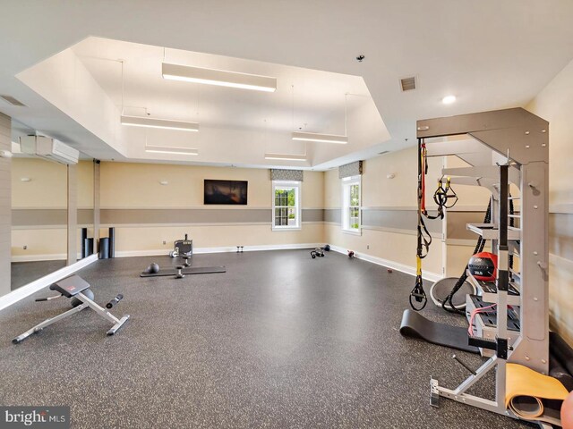 exercise room with visible vents, baseboards, and a wall mounted AC