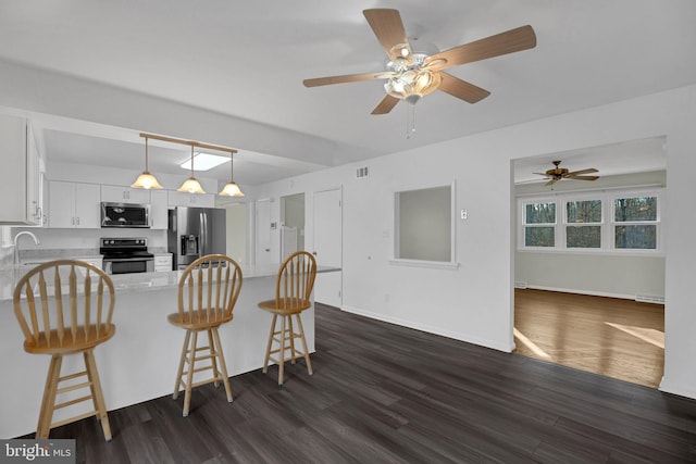 kitchen featuring white cabinetry, appliances with stainless steel finishes, a breakfast bar area, and dark hardwood / wood-style flooring