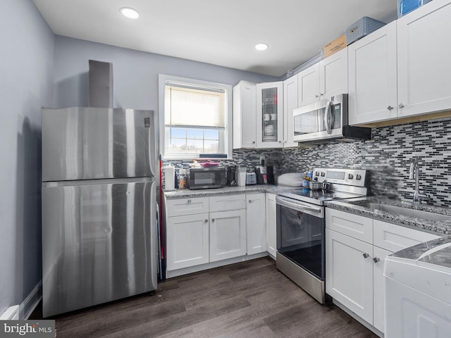 kitchen featuring dark wood finished floors, a sink, appliances with stainless steel finishes, white cabinetry, and tasteful backsplash