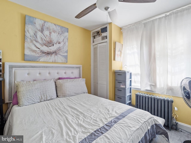 carpeted bedroom with a closet, baseboards, a ceiling fan, and radiator heating unit