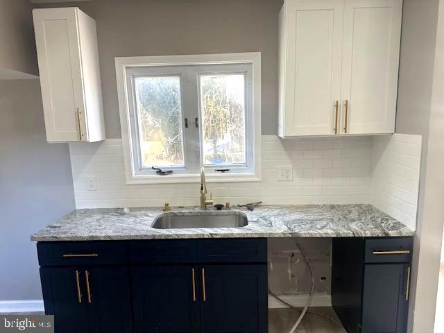 kitchen featuring sink, backsplash, light stone counters, white cabinets, and blue cabinets