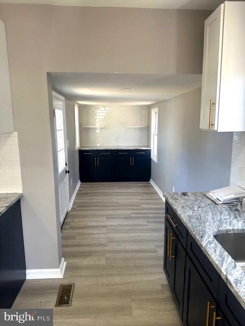 kitchen with white cabinetry, sink, decorative backsplash, light hardwood / wood-style floors, and light stone counters