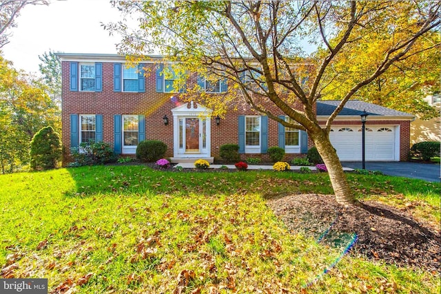 colonial inspired home with an attached garage, driveway, a front lawn, and brick siding