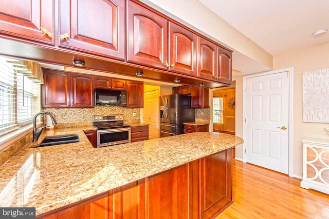 kitchen with light stone countertops, stainless steel appliances, dark brown cabinets, light wood-type flooring, and a sink