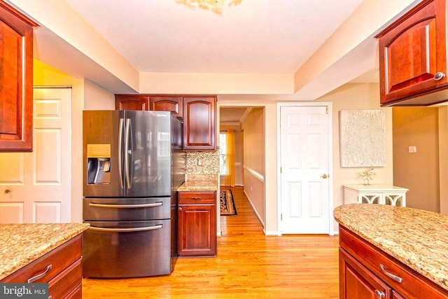 kitchen featuring light stone counters, light wood-style floors, dark brown cabinets, decorative backsplash, and stainless steel fridge