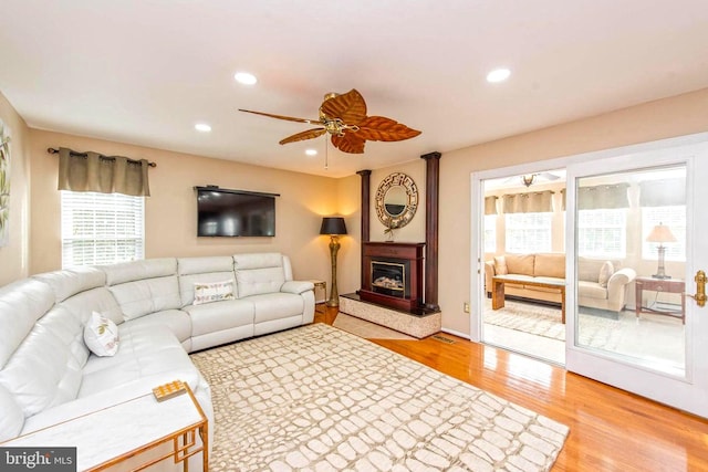 living area with ceiling fan, a glass covered fireplace, light wood-style flooring, and recessed lighting