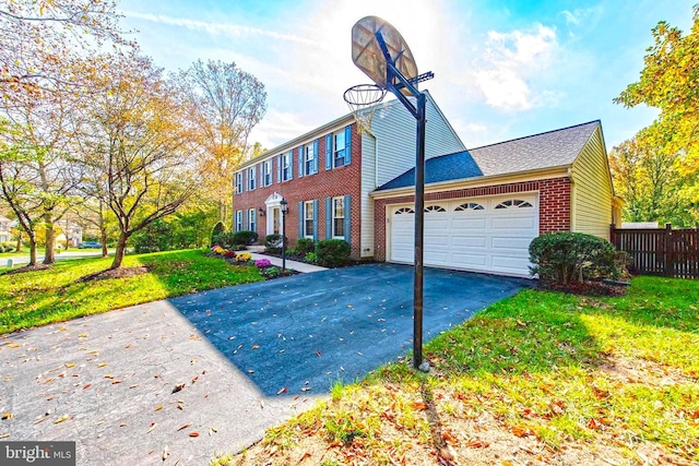 colonial home featuring an attached garage, brick siding, fence, driveway, and a front yard