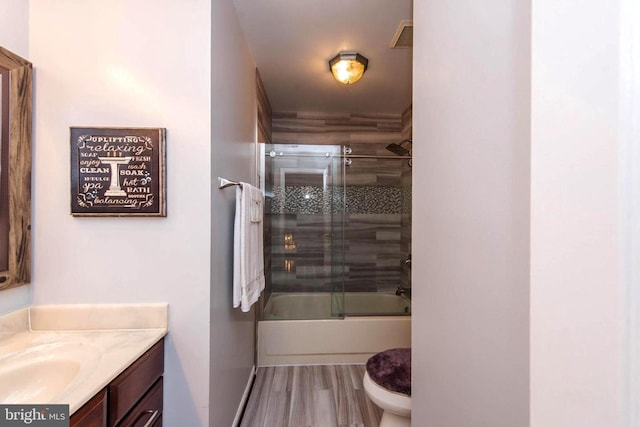 bathroom with visible vents, toilet, enclosed tub / shower combo, vanity, and wood finished floors