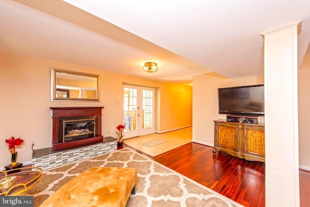 living area with french doors, a glass covered fireplace, and wood finished floors