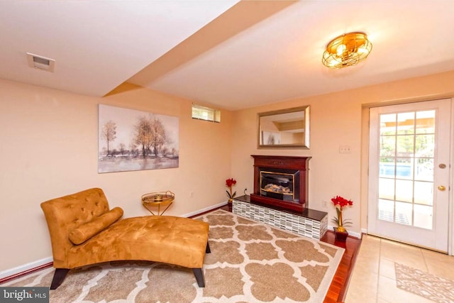 living area with tile patterned floors, baseboards, visible vents, and a glass covered fireplace