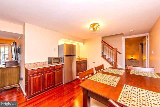 kitchen featuring reddish brown cabinets, appliances with stainless steel finishes, dark wood-type flooring, a sink, and light stone countertops