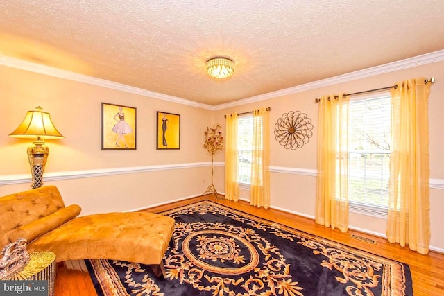 sitting room featuring a textured ceiling, wood finished floors, visible vents, and crown molding