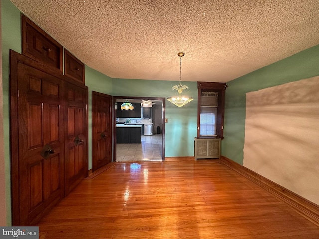 unfurnished dining area with light hardwood / wood-style floors, a textured ceiling, and a notable chandelier