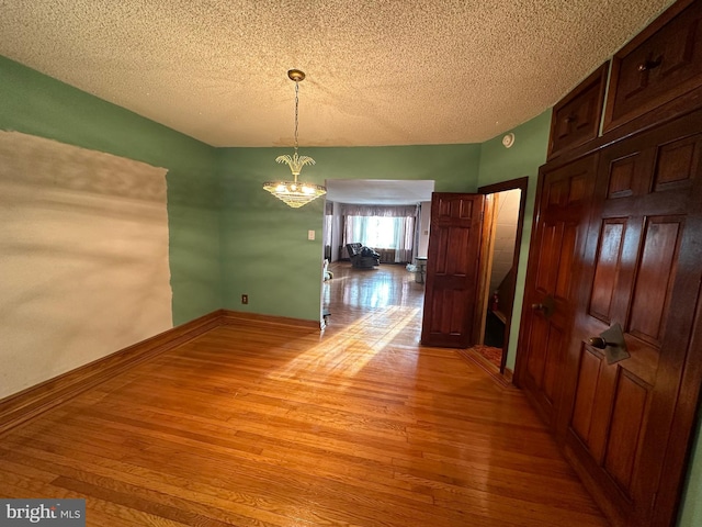 unfurnished dining area with a notable chandelier, wood-type flooring, and a textured ceiling