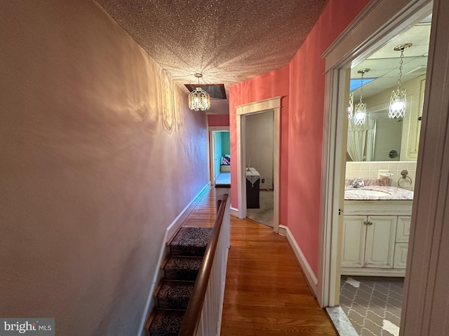 corridor with an inviting chandelier, hardwood / wood-style floors, sink, and a textured ceiling