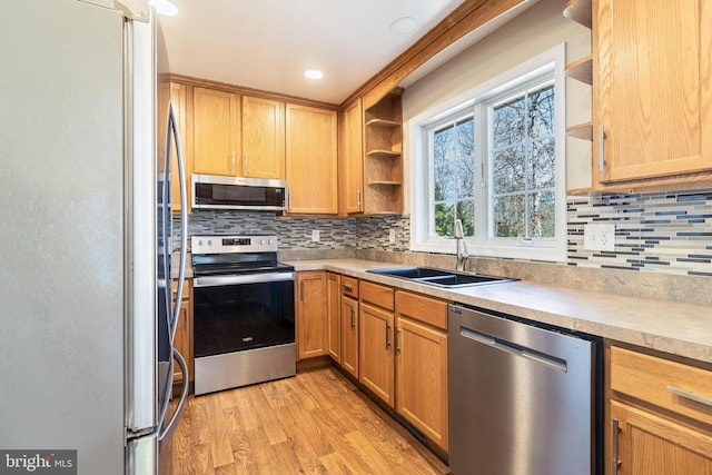 kitchen featuring open shelves, a sink, light wood-style floors, appliances with stainless steel finishes, and light countertops