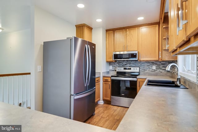 kitchen featuring light countertops, decorative backsplash, light wood-style flooring, stainless steel appliances, and a sink