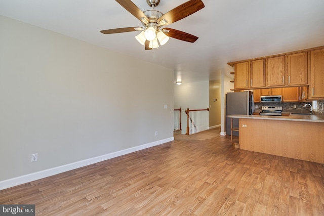 kitchen featuring a sink, light wood-style floors, appliances with stainless steel finishes, brown cabinetry, and decorative backsplash