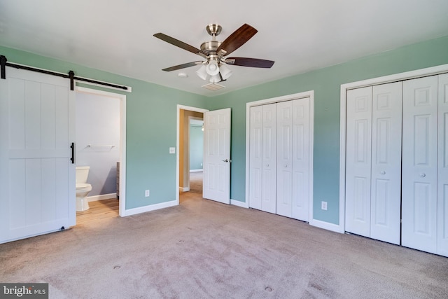 unfurnished bedroom with multiple closets, a barn door, connected bathroom, carpet flooring, and baseboards