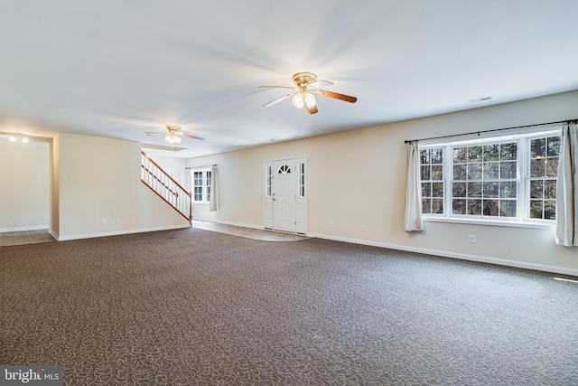 unfurnished living room featuring stairway, a ceiling fan, visible vents, and dark carpet