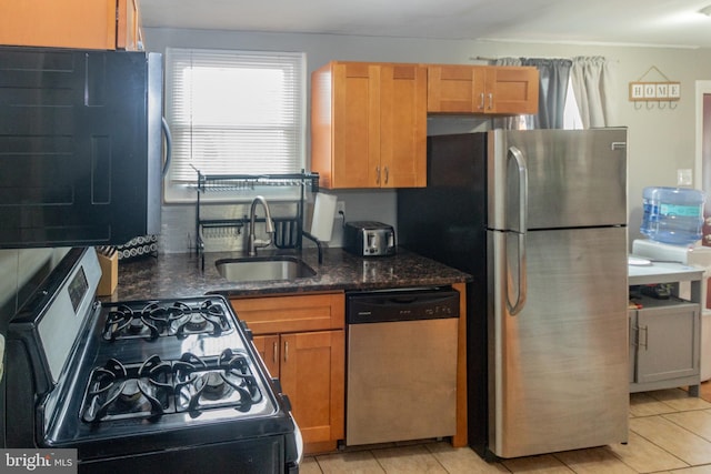 kitchen with sink, appliances with stainless steel finishes, dark stone counters, and light tile patterned floors