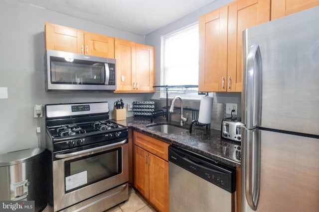 kitchen with sink, appliances with stainless steel finishes, dark stone counters, and light tile patterned flooring