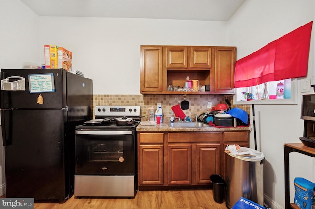 kitchen featuring stainless steel electric range oven, black refrigerator, tasteful backsplash, sink, and light hardwood / wood-style flooring