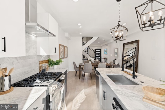 kitchen featuring white cabinets, stainless steel appliances, hanging light fixtures, and wall chimney exhaust hood