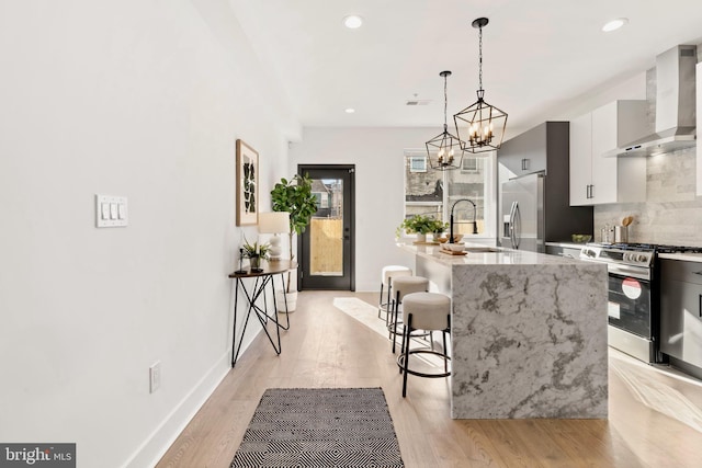 kitchen featuring a breakfast bar, sink, wall chimney range hood, stainless steel appliances, and a center island with sink