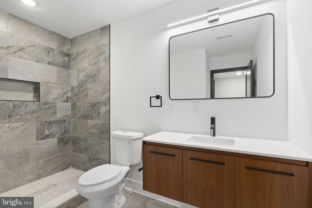 bathroom featuring vanity, toilet, and a tile shower