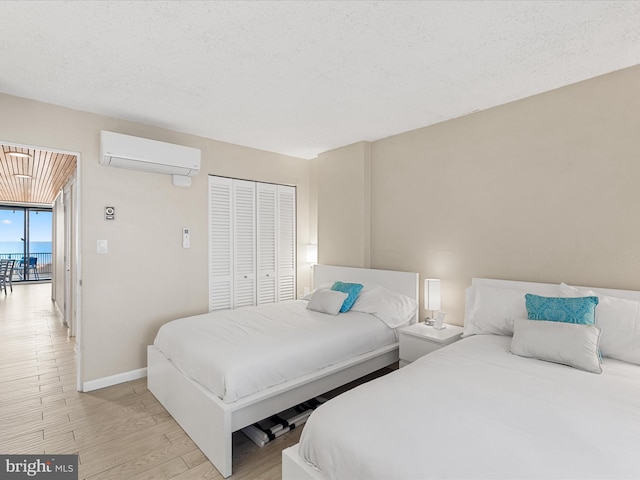 bedroom featuring a closet, a wall mounted air conditioner, a textured ceiling, and light wood-type flooring