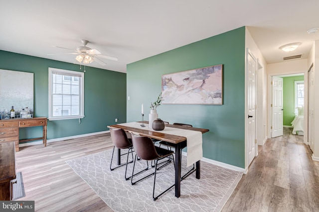 dining space with light wood finished floors, a ceiling fan, visible vents, and baseboards