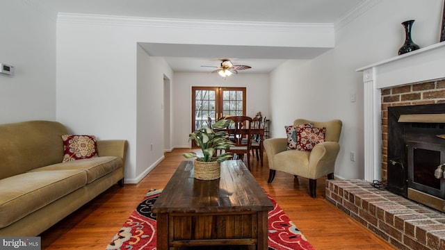 living room with a brick fireplace, crown molding, wood-type flooring, and ceiling fan