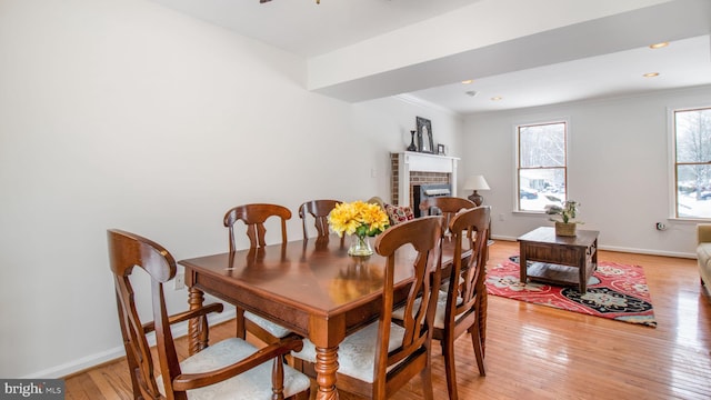 dining area featuring a brick fireplace, ornamental molding, and light hardwood / wood-style floors