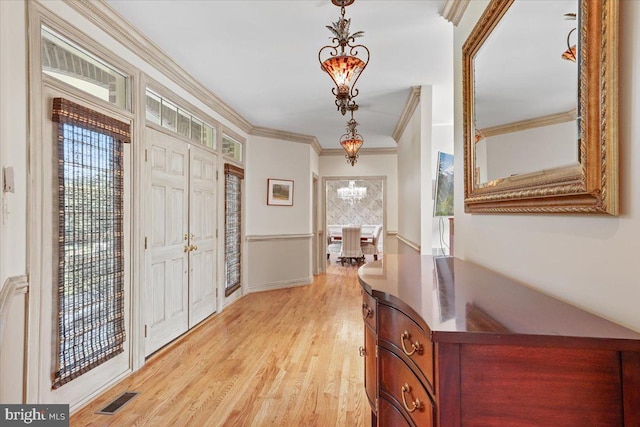 entrance foyer featuring visible vents, baseboards, ornamental molding, light wood-style floors, and a notable chandelier