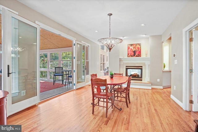 dining room featuring a multi sided fireplace, a chandelier, baseboards, and wood finished floors