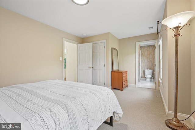 bedroom with visible vents, baseboards, light colored carpet, a closet, and ensuite bath