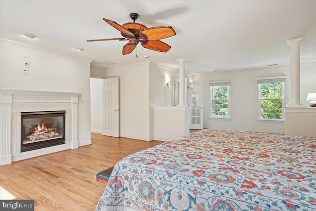 bedroom with decorative columns, wood finished floors, a high end fireplace, and ornamental molding