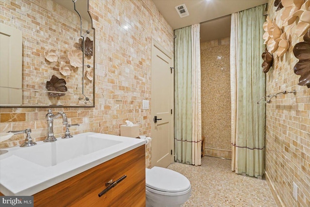 bathroom featuring vanity, toilet, visible vents, and brick wall