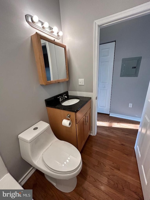 bathroom featuring wood-type flooring, toilet, electric panel, and vanity