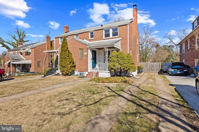 view of front of house with brick siding, fence, a chimney, and a front lawn