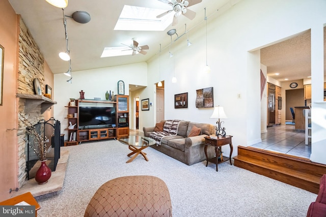 living area featuring a skylight, a ceiling fan, carpet, a stone fireplace, and high vaulted ceiling