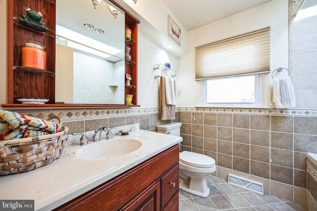 bathroom with tile patterned flooring, toilet, vanity, visible vents, and tile walls