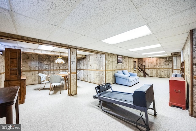 interior space featuring carpet floors, wooden walls, stairs, and a paneled ceiling