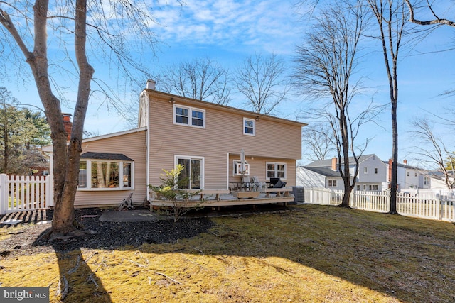 back of house featuring a chimney, a lawn, a sunroom, a fenced backyard, and a wooden deck