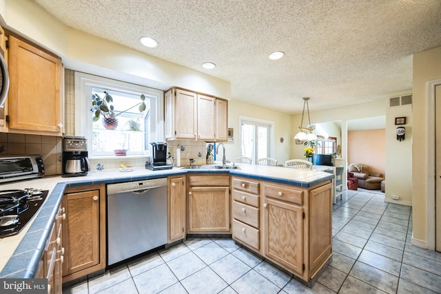 kitchen featuring tile counters, a sink, a peninsula, and stainless steel dishwasher